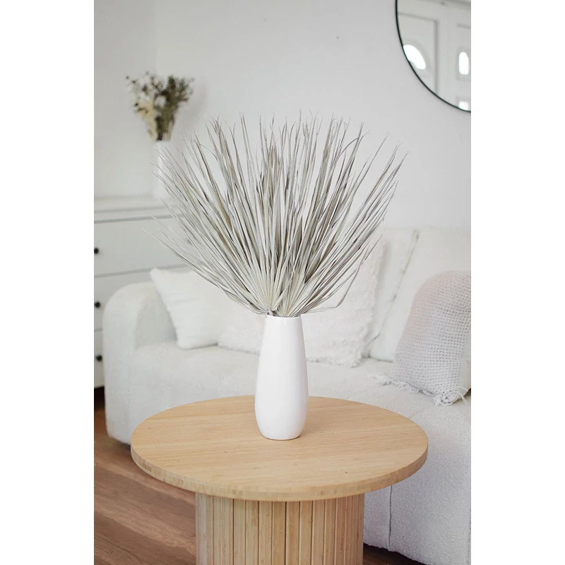 Szárított Chamaerops pálmalevél törtfehér színben, fehér vázában fa asztalon, világos enteriőrben